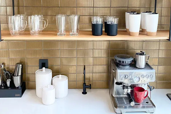 Coffee machine with a red mug on a white countertop against a gold tiled wall.