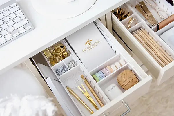 Organized desk drawer with stationery items on a white desk.