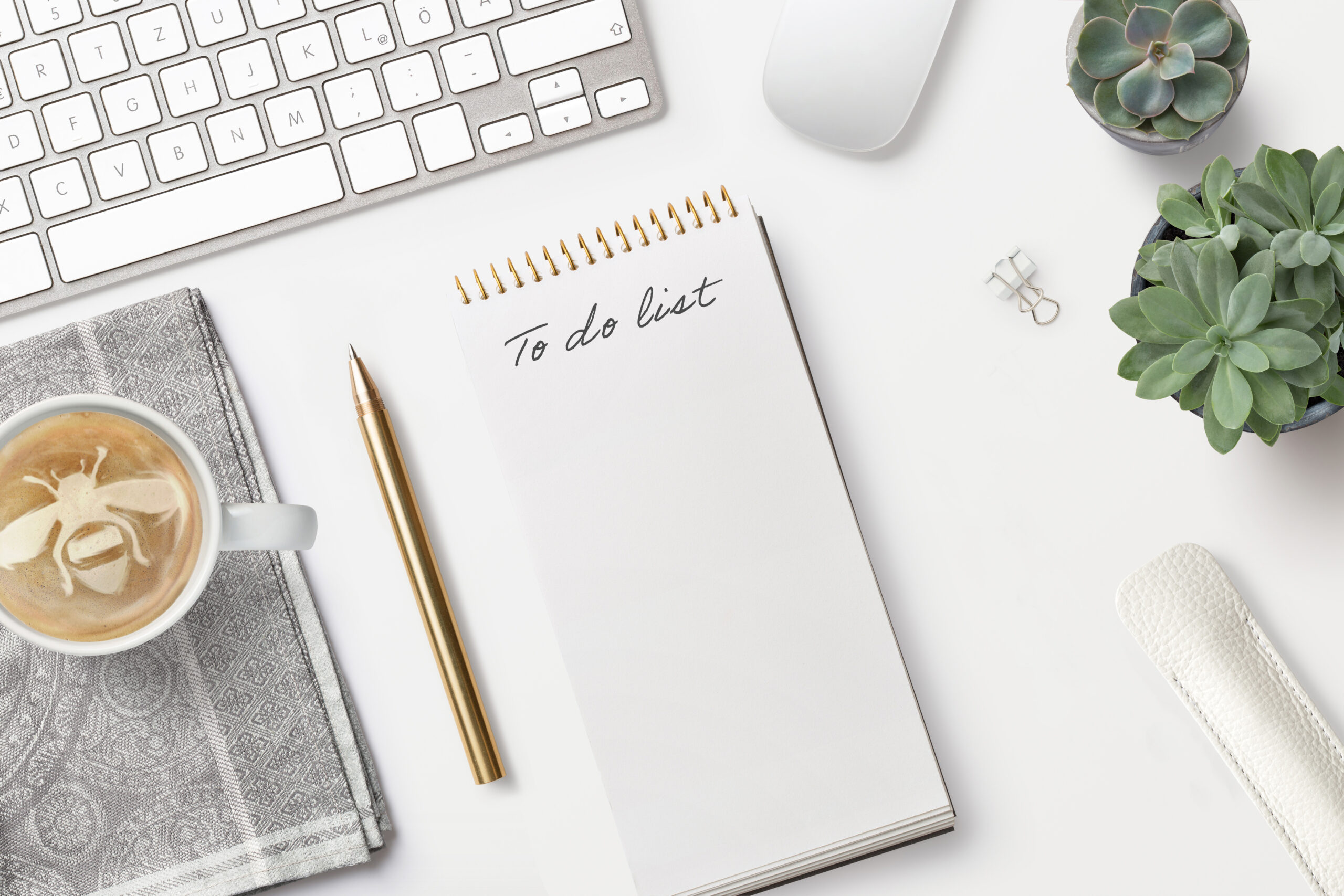 A note book with a to do list written on it and a pen lying next to it on a desk.